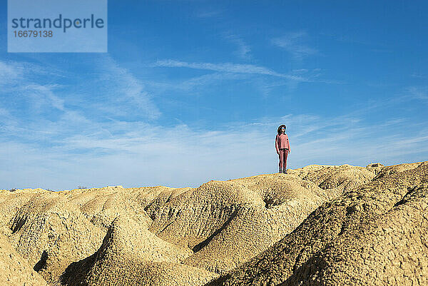 Schöne Frau mit Hut und Sonnenbrille steht auf Wüstendünen gegen blauen Himmel