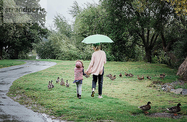 Mutter und Tochter gehen zusammen spazieren und halten sich an einem regnerischen Tag an den Händen