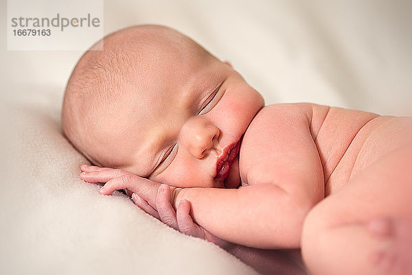 Vorderansicht eines neugeborenen Babys  das mit den Händen unter dem Kopf schläft