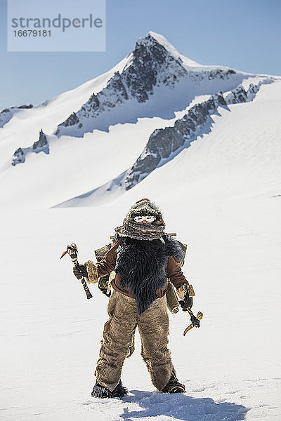 Jäger der Ureinwohner  der einen Pelz trägt und ein traditionelles Eispickelwerkzeug hält.