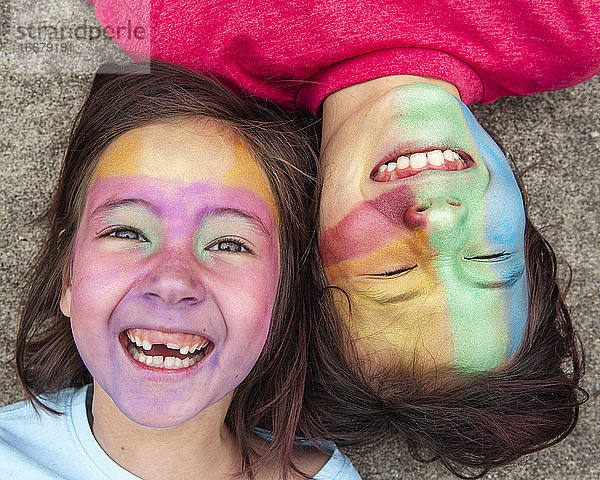Zwei Kinder liegen Wange an Wange mit bunter Gesichtsfarbe und lachen