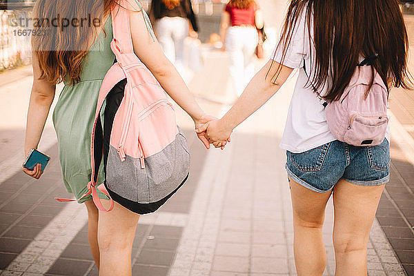 Rückansicht eines lesbischen Paares  das sich beim Spaziergang in der Stadt an den Händen hält