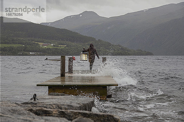 Eine Person mit einer Laterne an der Kante eines Docks in Norwegen