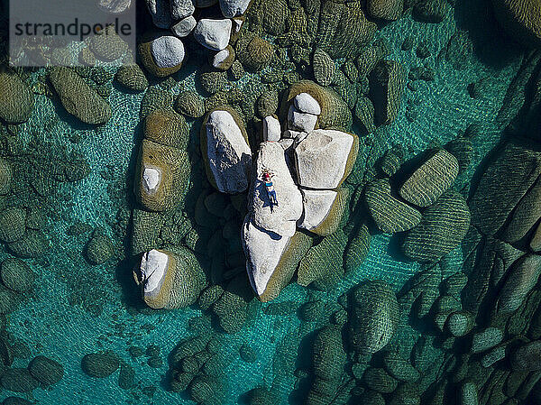 Drohnenaufnahme einer Frau  die sich an einem sonnigen Tag auf einem Felsen am Lake Tahoe entspannt
