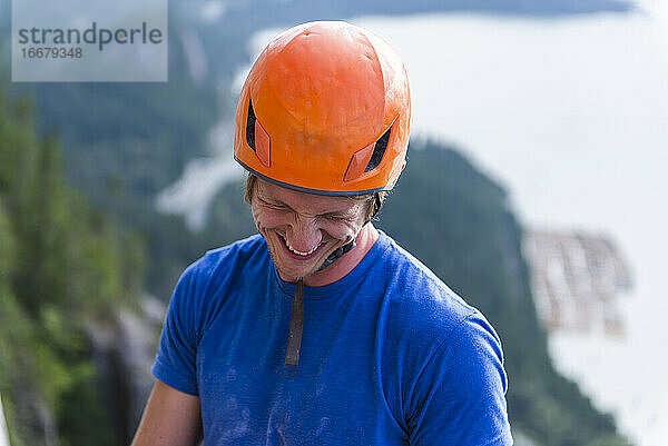 Kletterer mit Helm  der lächelnd und lachend über Wasser nach unten schaut