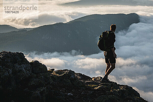 Männlicher Wanderer auf dem Gipfel blickt auf den Berg  der sich über den Wolken erhebt  Maine