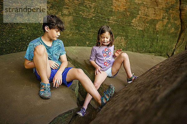 Zwei Kinder spielen zusammen auf einem großen Felsblock in der Nähe einer Sandsteinfelswand