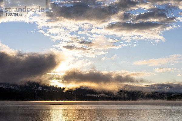 Sonnenaufgang über ruhigen See Wasser mit Wolken und Bäume in der Landschaft