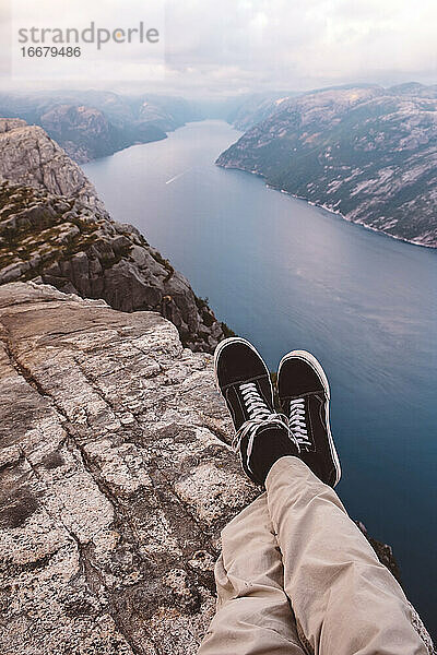 Person im Schneidersitz am Rande einer Klippe mit Blick auf die Fjorde in Norwegen