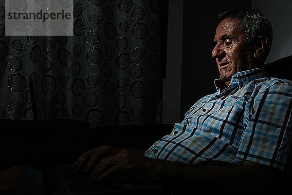 Älterer Mann surft auf einem Laptop in einem dunklen Raum