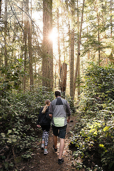 Vater und Tochter beim Wandern auf einem Waldweg an einem sonnigen Tag
