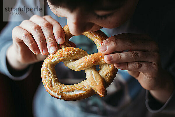 Nahaufnahme eines Jungen  der eine weiche  selbstgebackene Brezel isst.