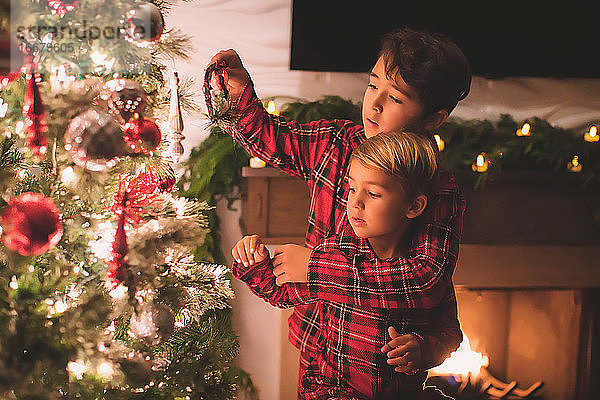 Zwei Brüder hängen nachts Ornamente an den Weihnachtsbaum