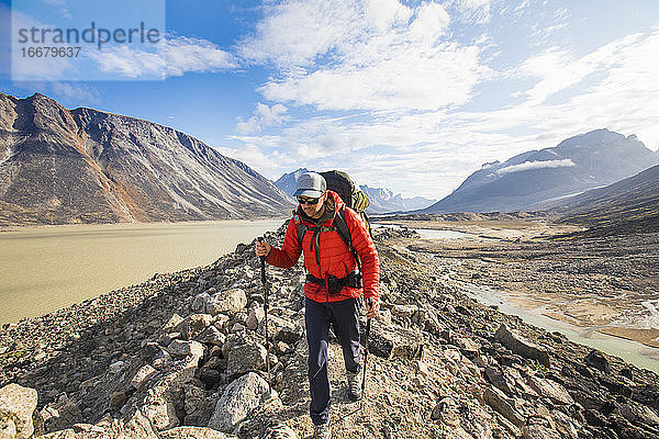 Rucksacktourist mit warmer roter Jacke beim Wandern über unwegsames Gelände.