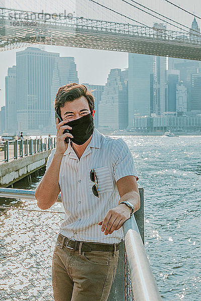 Junger Mann am Fluss mit Gesichtsmaske und Telefon.