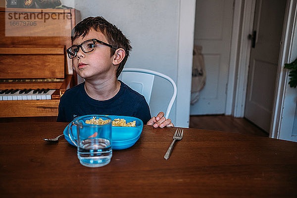 Junge schaut während einer Mahlzeit verärgert auf den Tisch