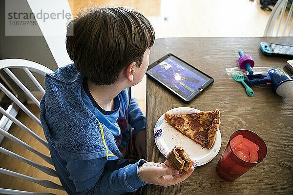 Overhead-Ansicht von Teenager-Junge mit Grippe Essen Pizza beobachten Ipad am Tisch