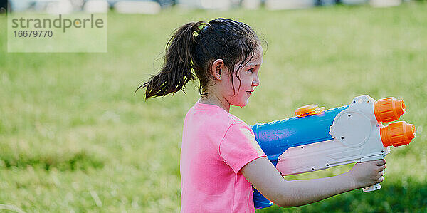 Mädchen spielt mit einer Wasserpistole im Garten und trägt ein rosa T-Shirt