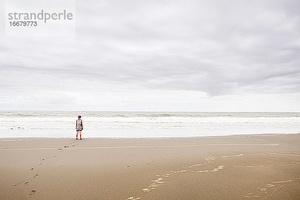 Junge steht am Strand und schaut auf das Wasser