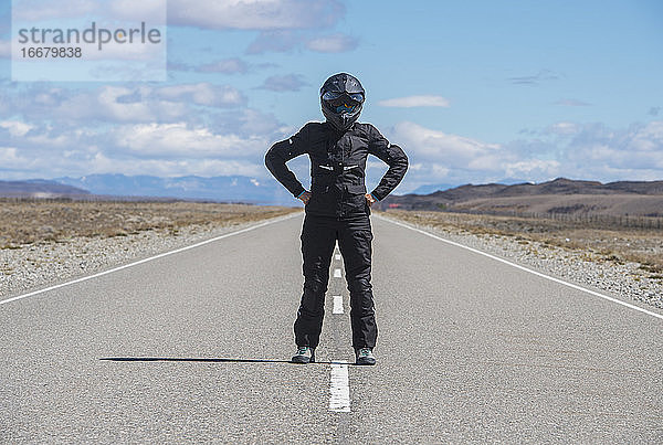 Frau in Motorradkleidung steht mitten auf der leeren Autobahn