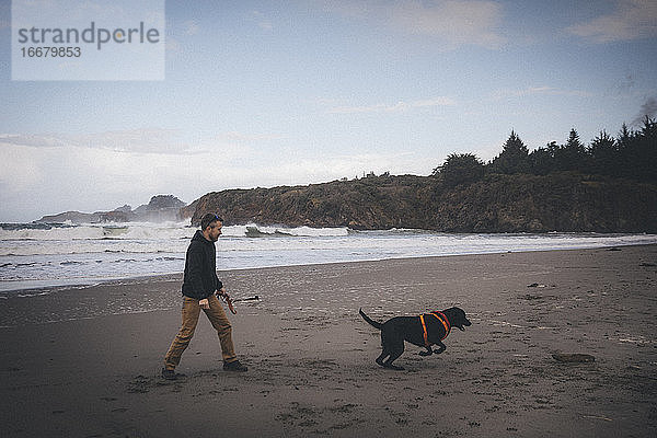 Ein Mann spielt mit einem Hund am kalifornischen Strand