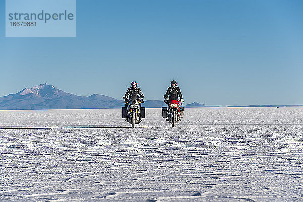 Zwei Männer fahren mit dem Motorrad über die Salinen von Uyuni