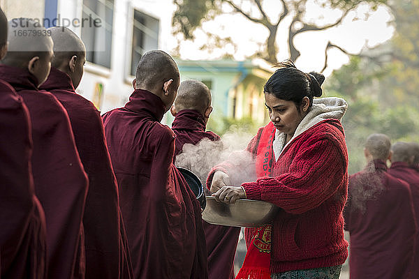 Eine burmesische Frau gibt gedämpften Reis an Mönche  die in der Schlange stehen  Nyaung U  Myanmar