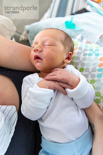 Neugeborenes Baby schläft friedlich in den Armen der Mutter.