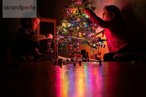 Geschwister schmücken ihren Weihnachtsbaum bei Nacht