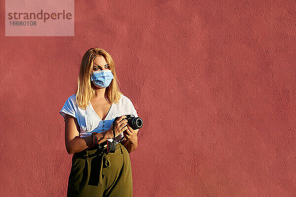 Junge Frau mit einer Maske und einer Kamera auf einem roten Hintergrund