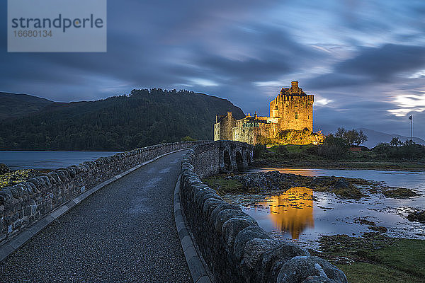 Beleuchtetes Eilean Donan Castle vor bewölktem Himmel in der Abenddämmerung  Schottland  UK