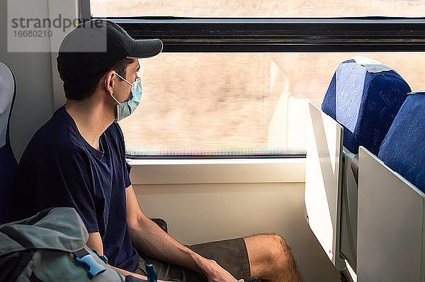 Junger Mann mit Maske  der während der Covid-19-Pandemie mit dem Zug reist.