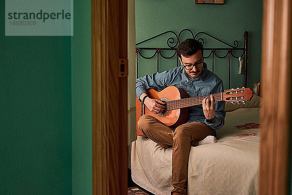 Junger Mann spielt Gitarre in einem Zimmer in seinem Haus