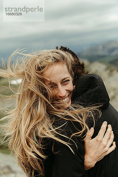 Frau mit langen blonden Haaren lacht und umarmt ihren Partner