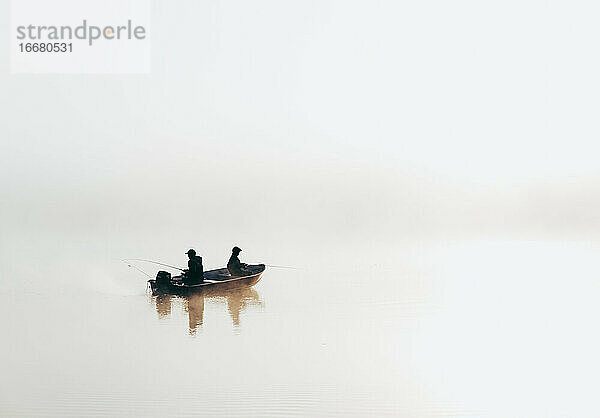 Mann und Kind beim Angeln in einem Boot bei dichtem Nebel auf einem See.