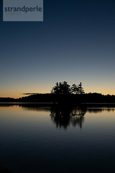 Silhouette von Bäumen auf einer Insel in einem See in Ontario bei Sonnenaufgang.