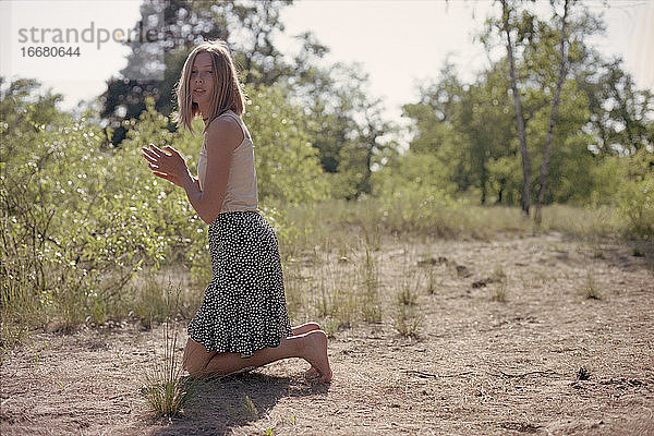 Blonde Frau im Rock steht an einem Fußweg im Frühlingswald.