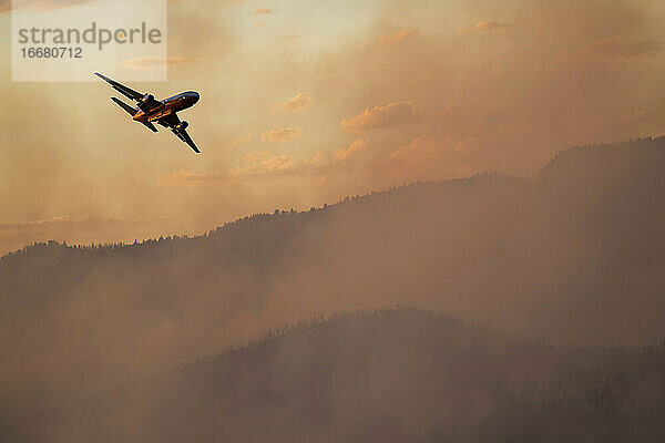 Militärflugzeug fliegt bei Sonnenuntergang über den Rauch eines Waldbrandes