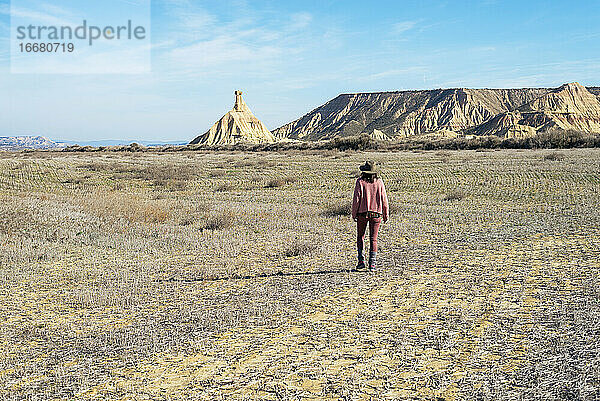 Rückansicht einer Frau in rosafarbener Kleidung  die an einem sonnigen Tag in einer Wüste spazieren geht