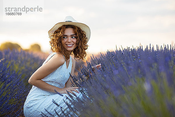 Frau mit lockigem Haar und Hut in einem Lavendelfeld