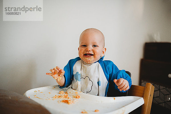 Nettes Baby lächelnd beim Essen mit seinen Händen mit schmutzigem Gesicht