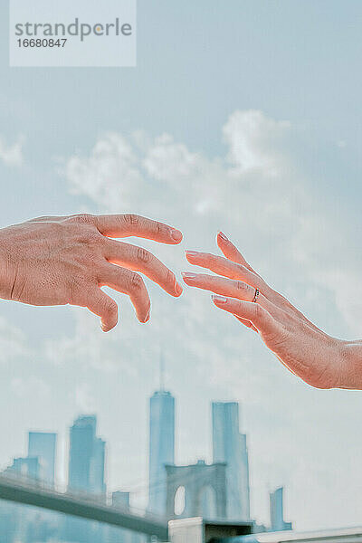Zwei Hände  die sich kaum berühren  gegen die Skyline.
