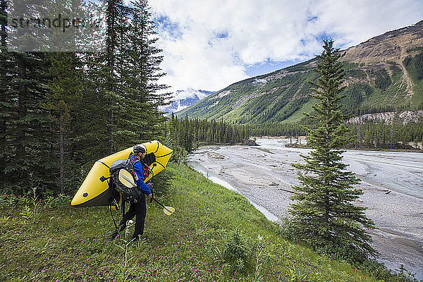Ein Forscher trägt ein Schlauchboot zum Fluss im Banff National Park hinunter.