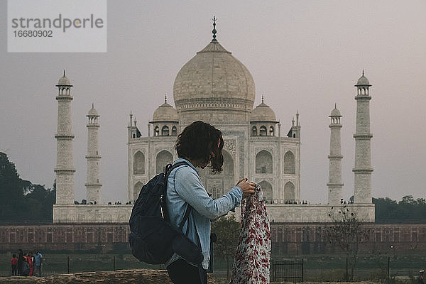 Junge Rucksacktouristin  die ihren Pashmina anzieht  bevor sie Mehtab Bagh verlässt  mit dem Taj Mahal im Hintergrund.