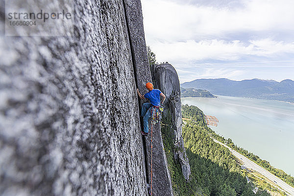 Seitenansicht eines Mannes beim Klettern einer Mehrseillängenroute auf einem Pfeiler mit Blick aufs Meer