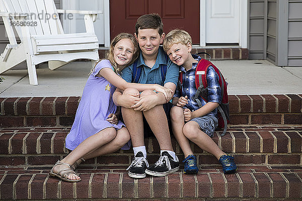Drei lächelnde Geschwister sitzen auf einer gemauerten Verandatreppe
