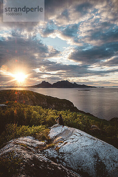Mann sitzt auf einem Felsen und schaut auf eine Berginsel bei Sonnenuntergang