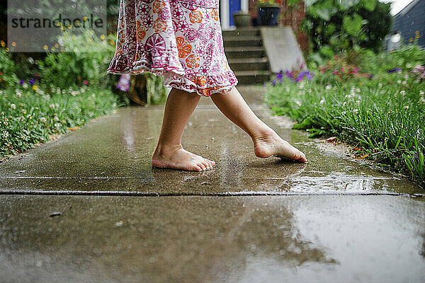 Nahaufnahme eines kleinen barfuß tanzenden Kindes auf der Treppe im Regen