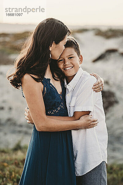 Schöne Mutter umarmt zärtlich gut aussehend preteen Sohn am Strand
