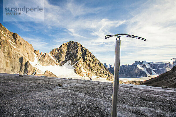 Bergsteiger mit Eispickel vor einem Gletscher und Bergen.